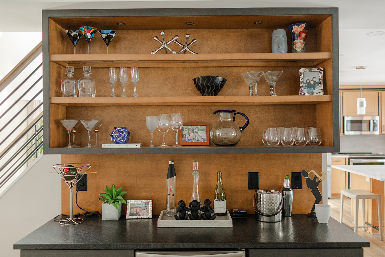 Built-in wooden bar and shelving unit with glass racks, dark countertop, and decorative glassware in a contemporary home remodeling interior.